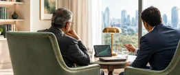 An adviser at a laptop while a client looks out over the city